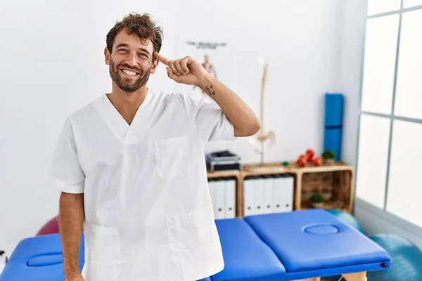 Young Handsome Physiotherapist Man Working Pain Recovery Clinic Smiling Pointing — Φωτογραφία Αρχείου