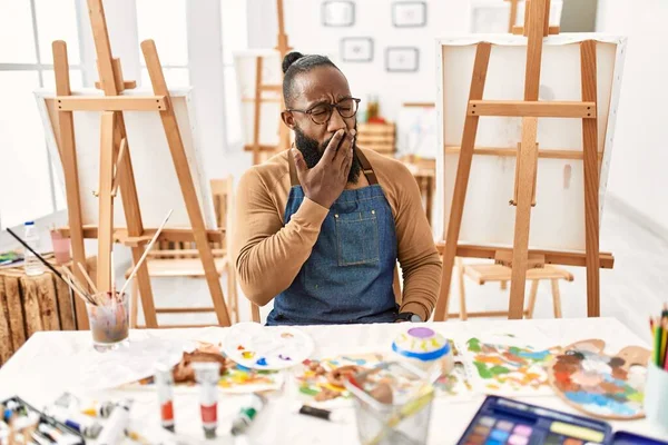 African american artist man at art studio bored yawning tired covering mouth with hand. restless and sleepiness. 