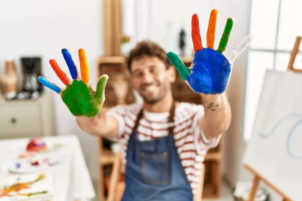 年轻的惊慌失措的男人自信地微笑着 在艺术工作室展示着彩色的手掌 — 图库照片