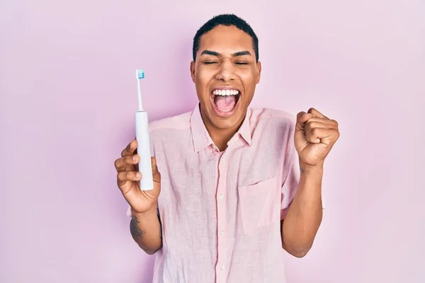 Young African American Guy Holding Electric Toothbrush Screaming Proud Celebrating — Stock Photo, Image