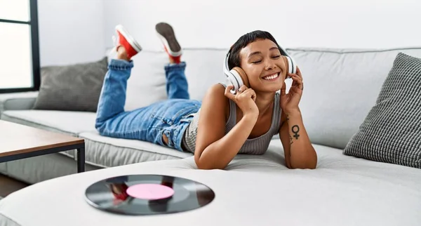 在家里沙发上躺着听音乐的年轻女人 — 图库照片