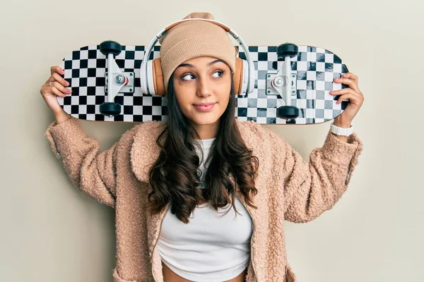 Young Hispanic Woman Holding Skate Wearing Headphones Smiling Looking Side — Stockfoto