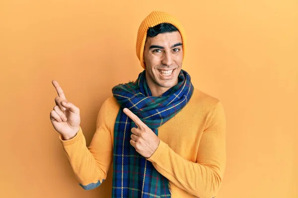 2本の手と指で側面を指しているカメラを見て笑顔と冬のスカーフを着てハンサムなヒスパニック系の男 — ストック写真