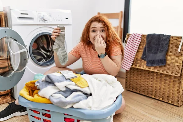 若いです赤毛の女性は手で口をカバー洗濯機笑いと恥ずかしがり屋のクスクス笑いに汚れた洗濯機を入れて ゴシップやスキャンダルの概念 — ストック写真