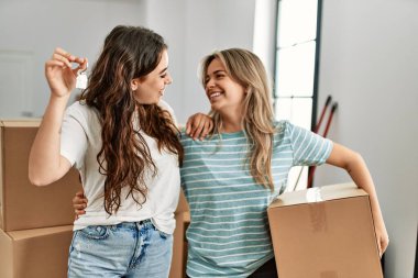 Mutlu bir şekilde gülümseyen genç çift yeni evin anahtarını ve karton kutuyu tutuyor..