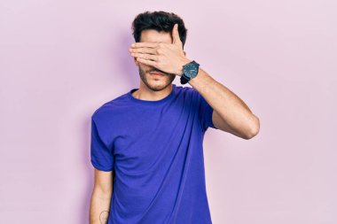 Gündelik tişörtler giyen genç İspanyol bir adam. Elle gözlerini kapatıyor. Ciddi ve üzgün görünüyor. Görme, saklama ve reddetme konsepti 