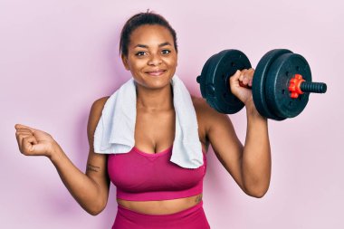 Spor kıyafetleri giyen Afrikalı genç bir kız dambılları kullanarak gururla bağırıyor, zaferi ve başarıyı kutluyor. 