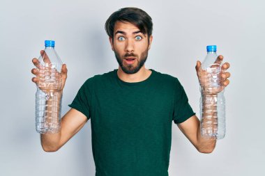 Plastik şişeleri geri dönüşüm için tutan genç İspanyol adam şaşkınlık ve şaşkınlık dolu bir ifade, korku ve heyecan dolu bir yüz ile şok oldu ve korktu.. 