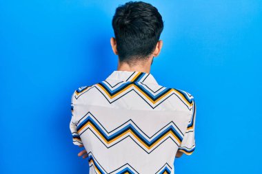 Gündelik kıyafetler giyen genç İspanyol adam arkasını dönüp kollarını kavuşturarak başka tarafa bakıyor. 