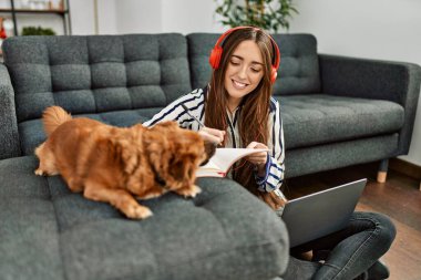 Genç İspanyol kadın dizüstü bilgisayar kullanıyor. Evde köpekle oturuyor.