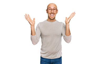 Bald man with beard wearing casual clothes and glasses celebrating crazy and amazed for success with arms raised and open eyes screaming excited. winner concept 