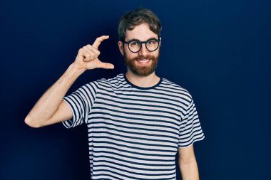 Beyaz, sakallı, çizgili tişörtlü, gözlüklü, gülümseyen, kendine güvenen, el hareketi yapan, parmakları küçük gösteren ve kameraya bakan bir adam. ölçüm kavramı. 
