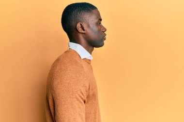 Afro-Amerikalı genç bir adam günlük giysiler giymiş, rahat bir görünüm takınıyor, doğal bir yüz ifadesi ve kendine güvenen bir gülümsemeyle poz veriyor.. 