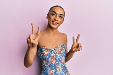 Makyajlı, uzun saçlı, zarif bir korse takmış kameraya bakıp zafer işareti yapan İspanyol bir adam. İki numara.. 