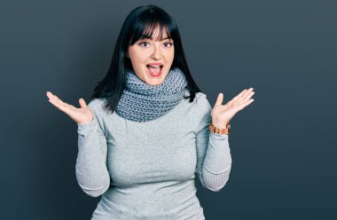 Genç Latin asıllı, uzun boylu, kış eşarbı takan bir kadın çılgın kutlamalar yapıyor ve başarıya hayret ediyor. Kolları açık, gözleri açık, heyecanla bağırıyor. Kazanan konsept 