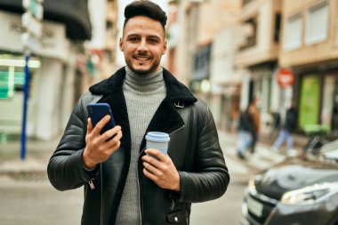 Genç Arap adam akıllı telefon kullanıyor ve şehirde kahve içiyor..