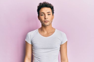 Young handsome man wearing casual white t shirt relaxed with serious expression on face. simple and natural looking at the camera. 