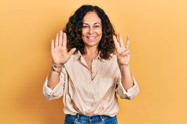 Orta yaşlı İspanyol kadın gündelik giysiler giyer ve 8 numaralı parmaklarıyla işaret ederken kendinden emin ve mutlu bir şekilde gülümser.. 