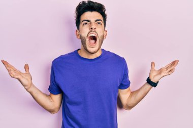 Günlük tişört giyen genç İspanyol adam deli gibi bağırıyor, agresif bir ifadeyle bağırıyor ve kollarını kaldırıyor. hüsran kavramı. 