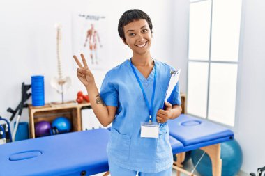 Kısa saçlı, İspanyol bir kadın ağrı kesici kliniğinde çalışıyor. Gülümsüyor ve parmaklarını zafer işareti yaparken kameraya bakıyor. İki numara.. 