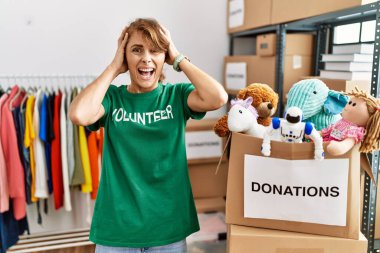 Bağışta gönüllü tişört giyen beyaz güzel bir kadın elleri başının üstünde, korkmuş ve ağzı açık bir şekilde şok geçirmekten korkan deli gibi duruyor. 