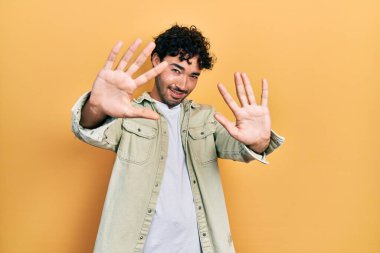 Gündelik kıyafetler giyen genç İspanyol adam on numarayı gösterip işaret ederken kendinden emin ve mutlu bir şekilde gülümsüyor.. 