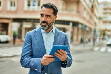 Orta yaşlı işadamı şehirde dokunmatik ped kullanarak mutlu bir şekilde gülümsüyor..