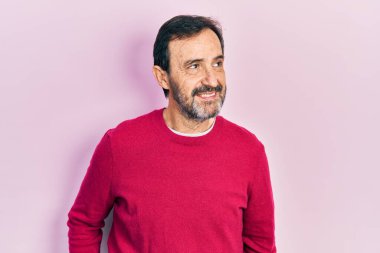 Orta yaşlı, sıradan kıyafetler giyen, yüzünde gülümsemeyle yan yana bakan İspanyol bir adam, doğal bir ifade. Kendinden emin gülen. 