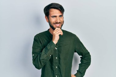 Gündelik giysiler giyen genç İspanyol adam kameraya kollarını kavuşturup çenesine dokunarak gülümsüyor. Olumlu düşünmek. 