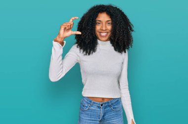 Genç Afro-Amerikan kızı, günlük kıyafetler giymiş, gülümseyen ve kendine güvenen, el hareketi yapan, parmaklarıyla işaret yapan ve kameraya bakan. ölçüm kavramı. 