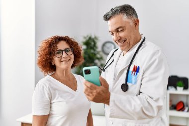 Orta yaşlı erkek ve kadın doktor üniforması giyiyor. Akıllı telefon kullanıyor. Klinikte tıbbi danışmanlık yapıyorlar.