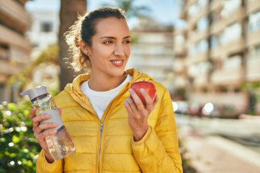 Genç İspanyol kız şehirde bir şişe su içip elma yiyor..