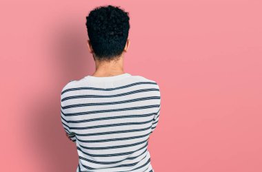 Young arab man with beard wearing casual striped sweater standing backwards looking away with crossed arms 