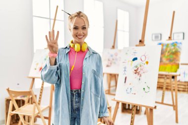 Young caucasian girl at art studio showing and pointing up with fingers number four while smiling confident and happy. 