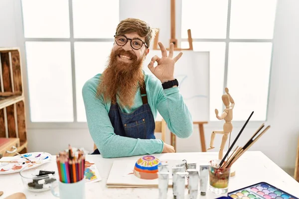 红头发的男人 留着长胡子 在艺术工作室里画着黏土碗 面带微笑 手指手画脚地签了名 成功表达 — 图库照片