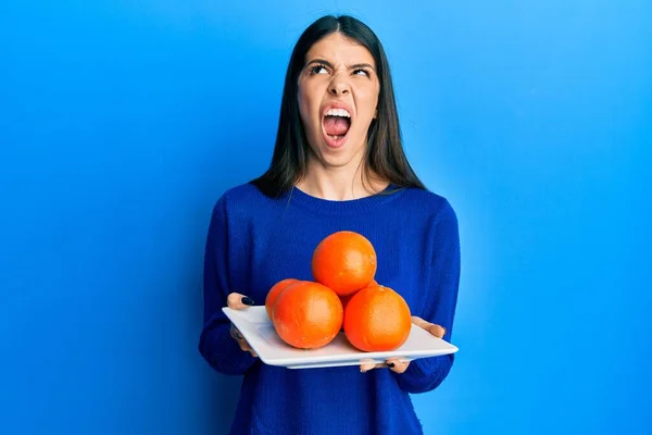Mujer Hispana Joven Sosteniendo Plato Con Naranjas Frescas Enojado Loco — Foto de Stock