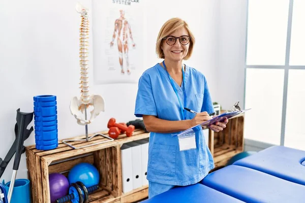 Mujer Rubia Mediana Edad Con Uniforme Fisioterapeuta Escribir Portapapeles Clínica —  Fotos de Stock