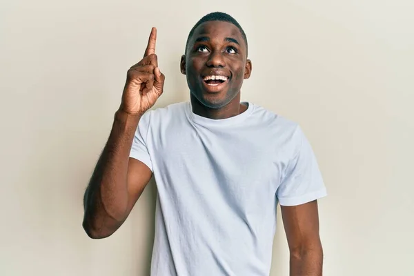 若いアフリカ系アメリカ人の男性は カジュアルな白いTシャツを着て成功したアイデアで指を指しています 興奮して幸せよ 第1位 — ストック写真