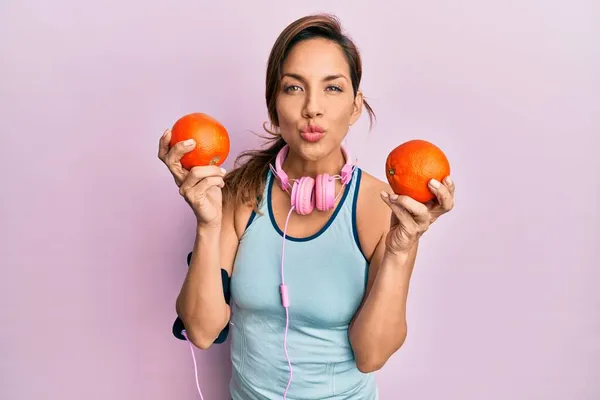 Молода Латинська Жінка Спортивному Одязі Використовуючи Навушники Тримаючи Апельсини Дивлячись — стокове фото