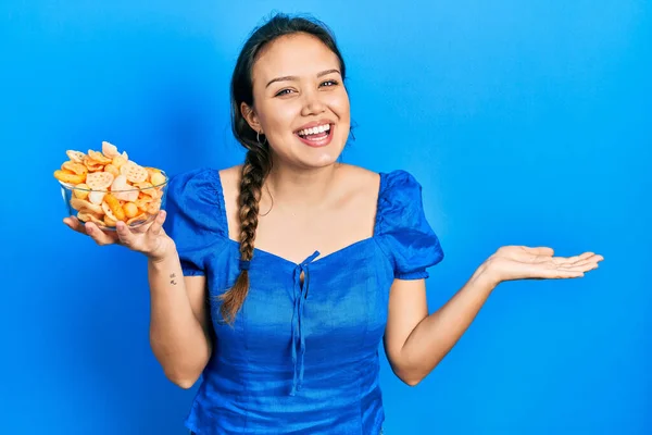 幸せな笑顔で達成を祝うポテトチップスのボウルを保持している若いヒスパニック系の女の子と勝者式とともに上げ手 — ストック写真