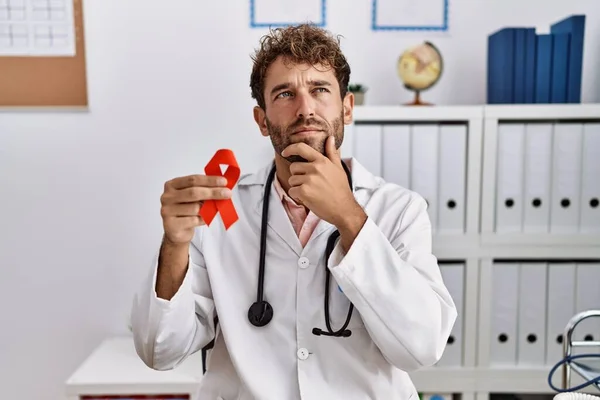 Young Hispanic Doctor Man Holding Support Red Ribbon Medical Clinic — Stok fotoğraf