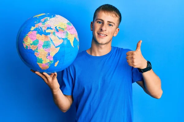 Young Caucasian Man Holding World Ball Smiling Happy Positive Thumb — Stock fotografie