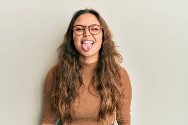 Günlük kıyafetler giyen ve gözlüklü genç İspanyol kız komik bir ifadeyle dilini dışarı çıkartıyor. duygu kavramı. 