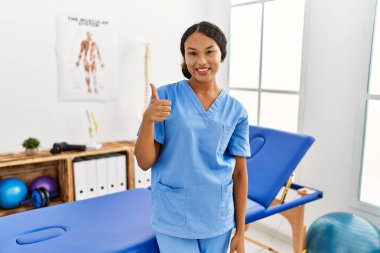 Ağrı kesici kliniğindeki güzel İspanyol fizyoterapist kadın elleriyle mutlu bir jest yapıyor. Kameraya bakıp başarıyı gösteren ifade. 