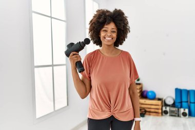 Genç Afrikalı Amerikalı kadın gülümsüyor spor merkezinde kendine güvenen bir perküsyon tabancası tutuyor.