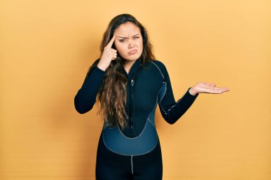 Genç İspanyol kız dalgıç neoprene üniforması giyiyor. Kafası karışmış ve avuç içi açık bir şekilde fotokopi alanını gösteriyor ve alnını işaret ediyor. Bunu bir düşün.. 