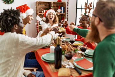 Bir grup genç, mutlu bir şekilde gülümseyerek evde Noel yemeği yiyor..