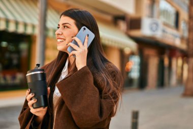 Genç İspanyol kadın akıllı telefondan konuşuyor ve şehirde kahve içiyor..
