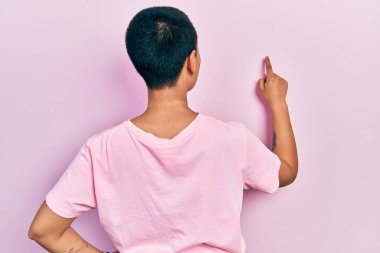 Kısa saçlı, sıradan pembe tişörtlü güzel bir İspanyol kadın parmak eliyle öne doğru poz veriyor. 