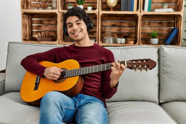 Evdeki kanepede oturan Latin kökenli genç adam klasik gitar çalıyor..